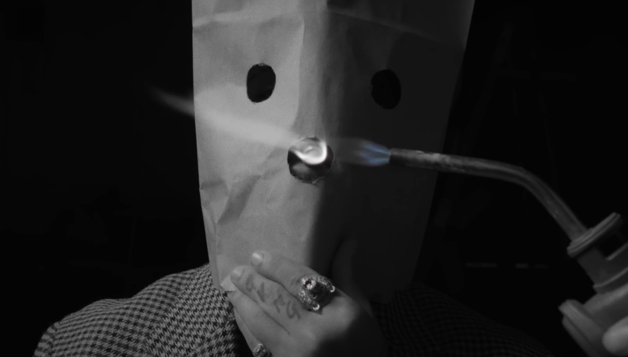 Black-and-white close-up of a paper mask and a small flame