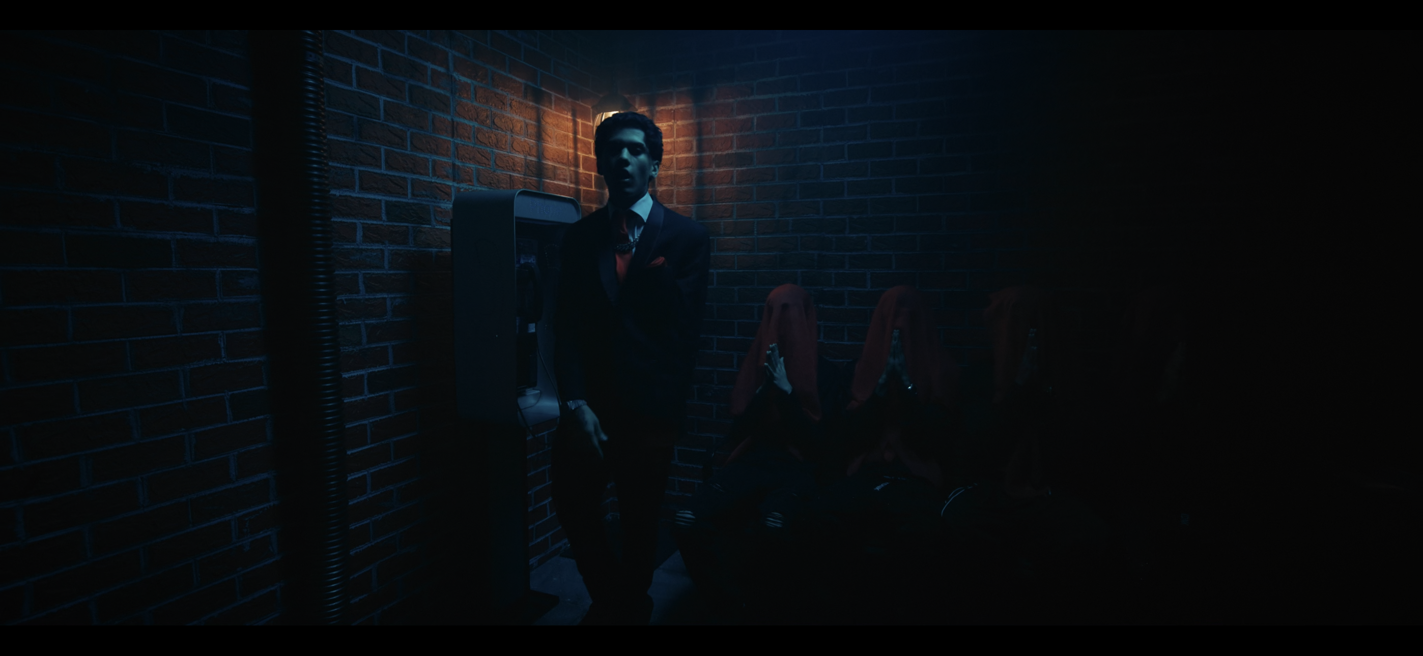 Blue-lit brick room with a suited figure and red-veiled figures